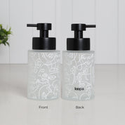 Front and back view of frosted glass soap dispenser with abstract face pattern wrap, 250ml refillable bathroom pump bottle featuring matte black stainless steel pump, modern reusable hand wash container with minimalist artistic design, eco friendly countertop accessory with subtle Loopa branding on reverse side