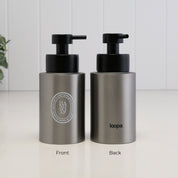 Two brushed stainless steel pump bottles shown side by side on a white surface against a white paneled wall. The left bottle shows the front with a circular logo reading HADSOAP, and the right bottle shows the back with the brand name loopa.