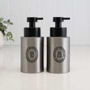 Pair of 250ml brushed 304 stainless steel hand soap and hand lotion dispensers with black oval labels and satin black liquid pumps, designed as a matching refillable bathroom or kitchen sink set.