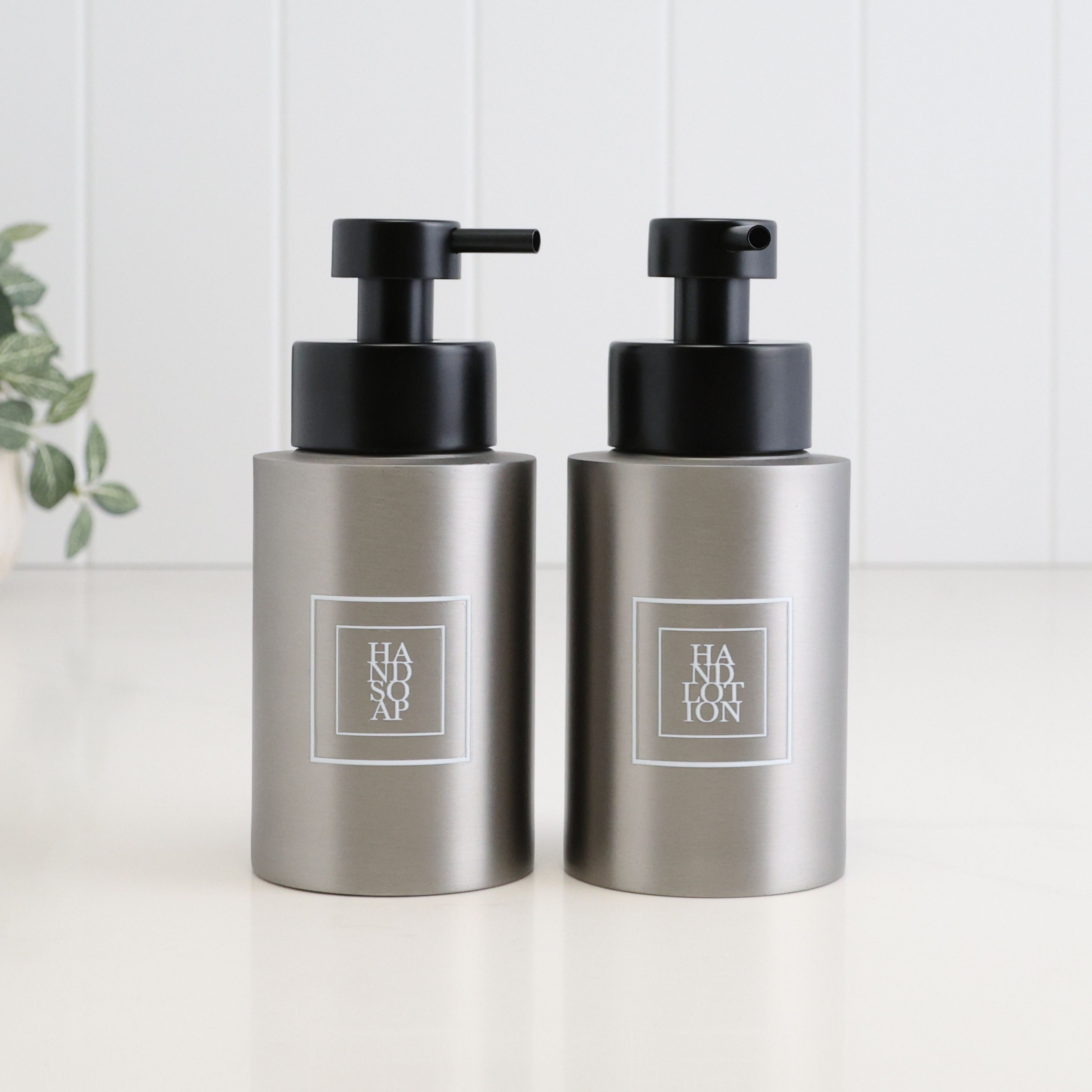 Pair of 250ml brushed 304 stainless steel dispensers for hand soap and hand lotion, finished with white square labels and satin black liquid pumps for a coordinated bathroom or sink set.