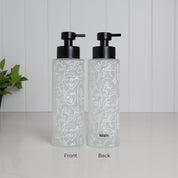 Front and back view of tall frosted glass dispenser with abstract face line art wrap, 500ml refillable bathroom pump bottle with matte black stainless steel top, modern reusable shampoo or body wash container, minimalist eco friendly glass design with subtle branding on reverse side