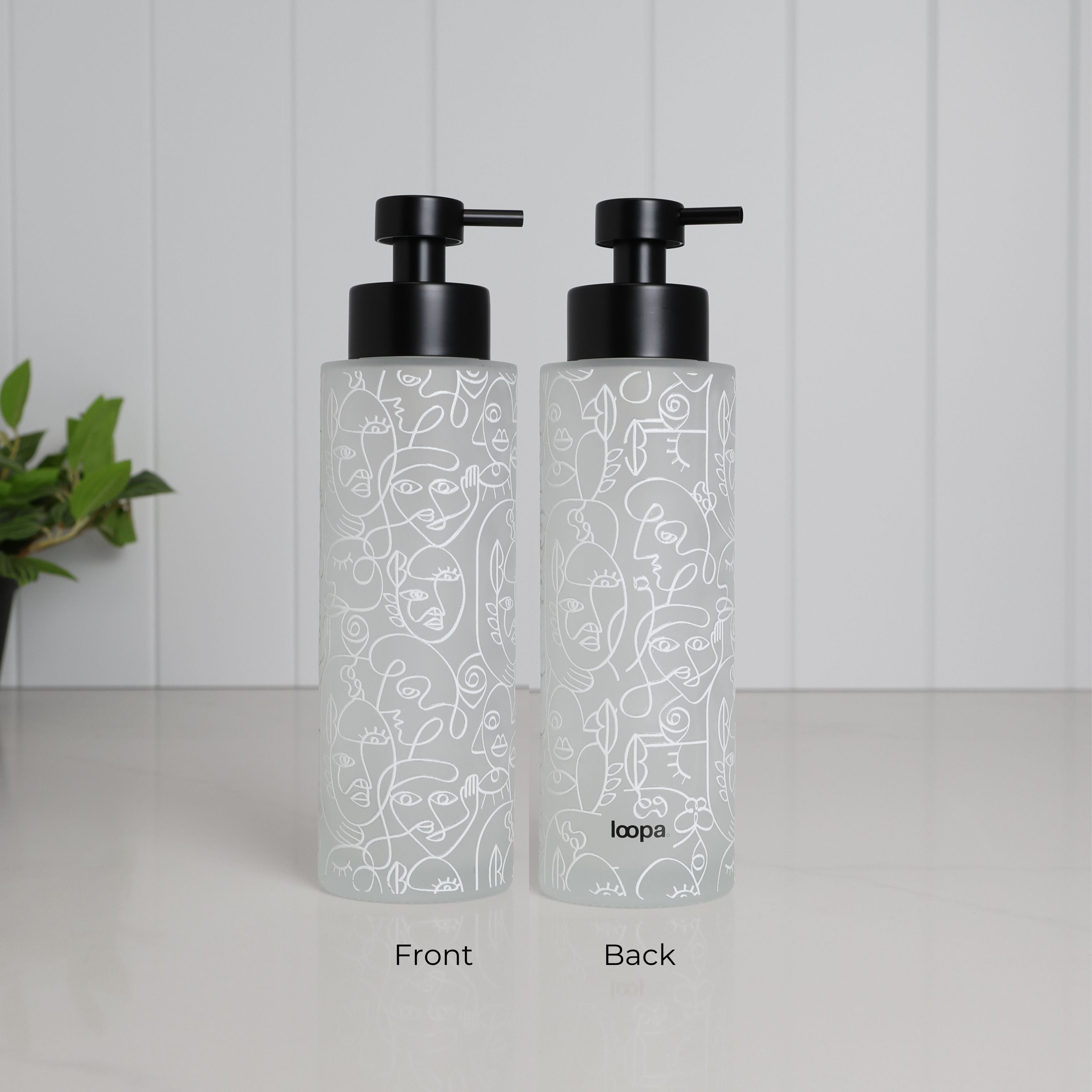 Front and back view of tall frosted glass dispenser with abstract face line art wrap, 500ml refillable bathroom pump bottle with matte black stainless steel top, modern reusable shampoo or body wash container, minimalist eco friendly glass design with subtle branding on reverse side