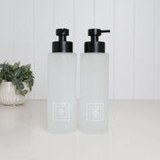 Set of two 500ml frosted glass soap dispensers with white Shampoo and Conditioner labels and satin black pumps, designed as matching refillable shampoo and conditioner bottles for a modern bathroom or shower.