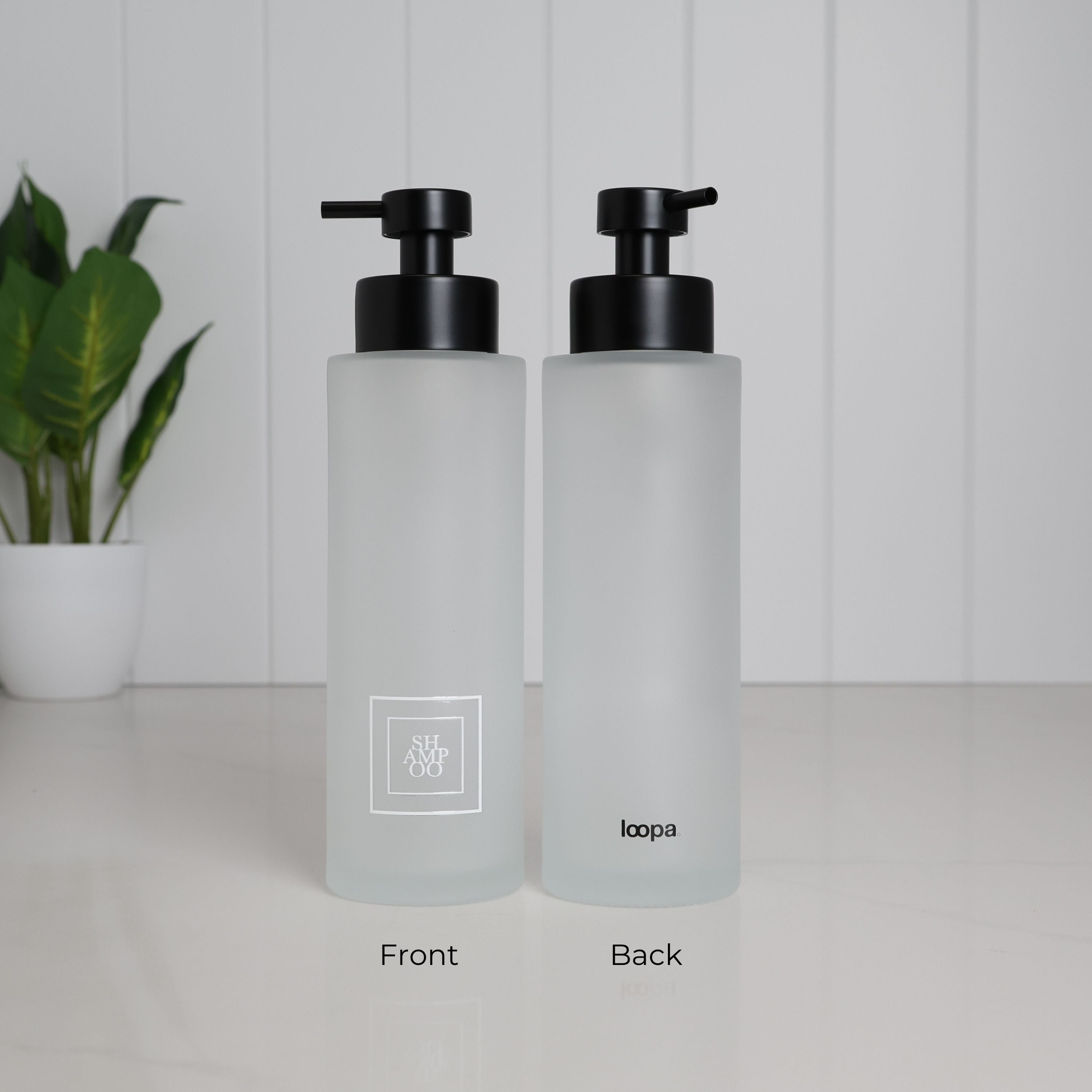 Front and back views of a 500ml frosted glass soap dispenser with white Shampoo label, satin black pump and Loopa branding, designed as a refillable shampoo bottle for a modern bathroom or shower.