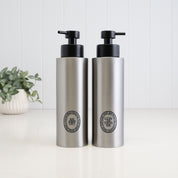 Pair of 500ml brushed 304 stainless steel refillable shampoo and conditioner dispensers with black oval labels and satin black liquid pumps, designed for coordinated bathroom and shower storage.