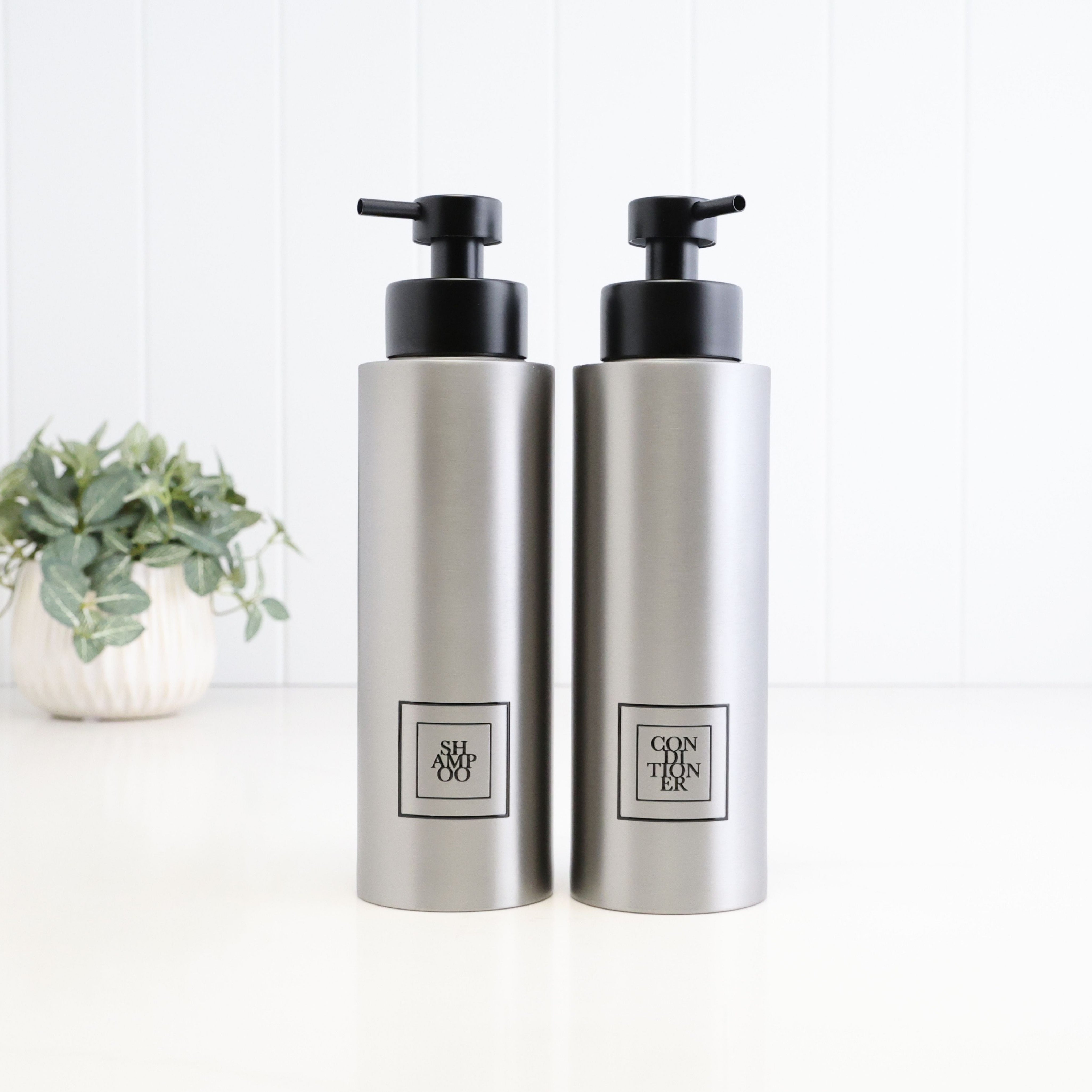 Pair of 500ml brushed 304 stainless steel shampoo and conditioner dispensers with black square labels and satin black pumps, designed as a matching refillable bathroom and shower bottle set.