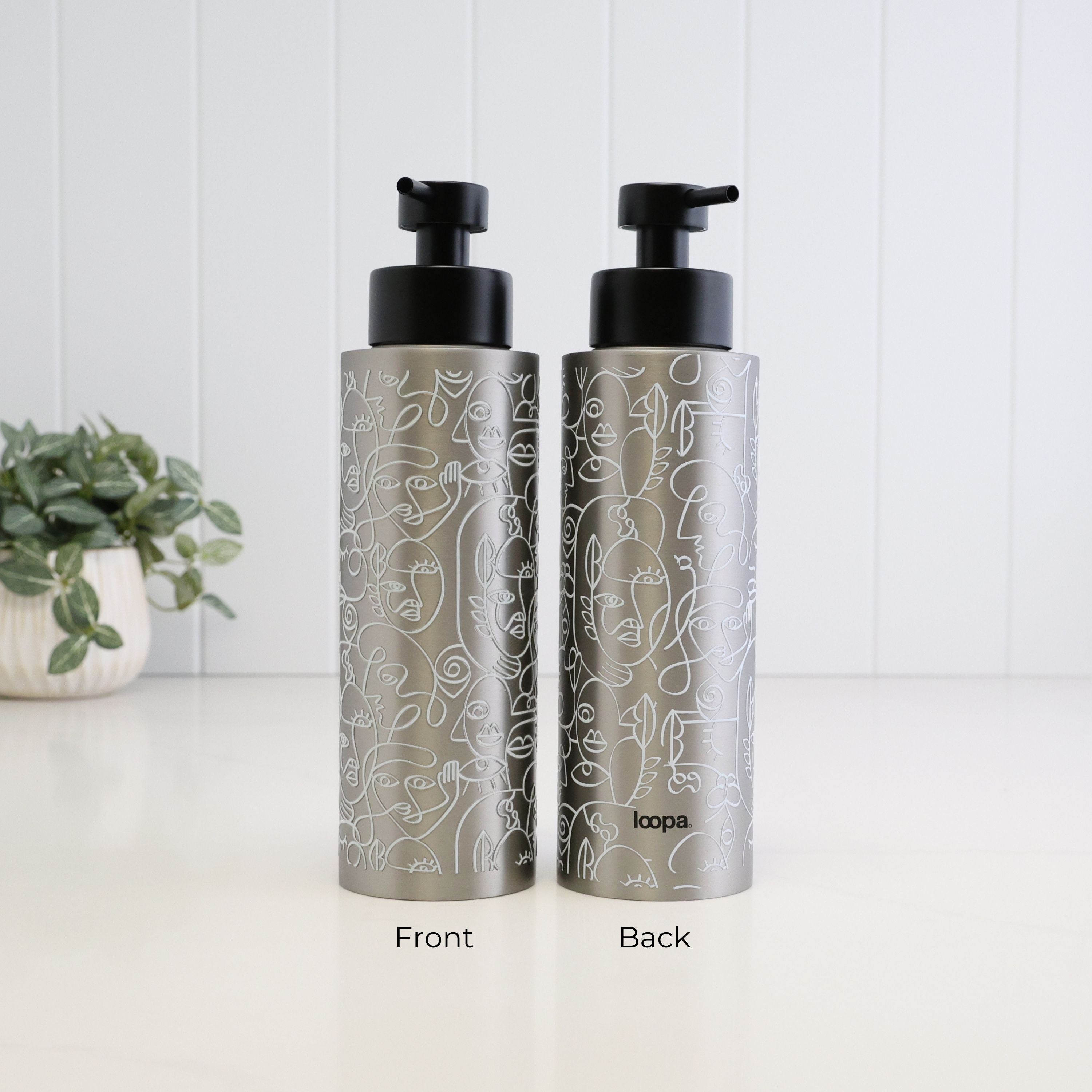 Front and back view of a 500ml brushed 304 stainless steel soap dispenser with white abstract face line art, satin black liquid pump and Loopa branding, showing the decorative wrap around the refillable bottle.