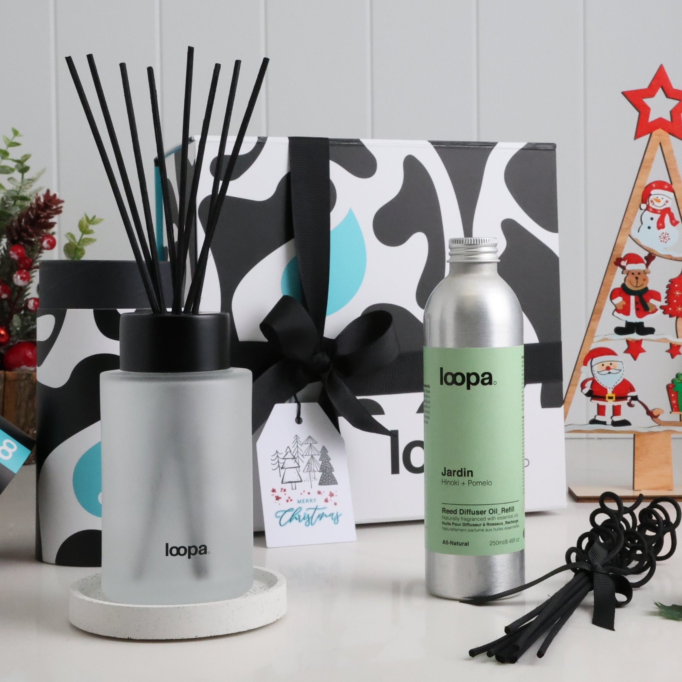 Frosted glass diffuser with straight black reeds shown next to Jardin refill oil and a ribbon-tied Christmas gift box. Surrounded by seasonal decorations, perfect for festive home scent gifting and winter ambience.