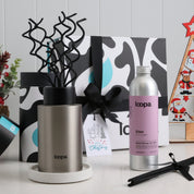Brushed steel diffuser with sculpted reeds paired with Eden refill, placed in front of a Christmas gift box and holiday ornaments. A stylish seasonal fragrance set suited for thoughtful Christmas gifting.
