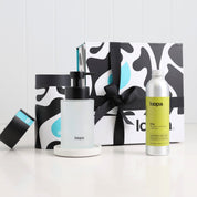 Frosted glass soap dispenser on a smooth terrazzo-style base paired with an Elio scented aluminium refill bottle, set against Loopa’s bold black-and-white gift box with ribbon for a clean, modern luxury gifting presentation.