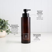 An amber brown pump bottle with a black dispenser, shown on a white surface against a white paneled wall. Text callouts describe product features, and a small green plant is visible on the left.
