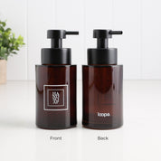 Two amber glass pump bottles shown side by side on a white surface, labeled Front and Back. The left bottle shows the front with a black pump and a white square logo reading HAND AP, and the right bottle shows the back with a black pump and the word loopa.