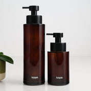 Two amber glass round bottle dispensers with a plain, unlabelled finish, shown together in 500ml and 250ml refillable sizes for kitchens, bathrooms, or utility spaces