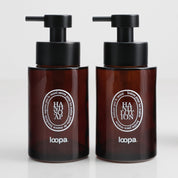 Two amber glass round bottle dispensers with white oval labels, presented as a coordinated 250ml refillable set for bathrooms, cloakrooms, or kitchen use