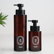 Two amber glass round bottle dispensers with white oval labels, shown together in 500ml and 250ml refillable sizes for soap or lotion use