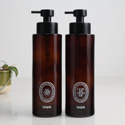 Two amber glass round bottle dispensers with white oval labels, presented as matching 500ml refillable options for soap or lotion use