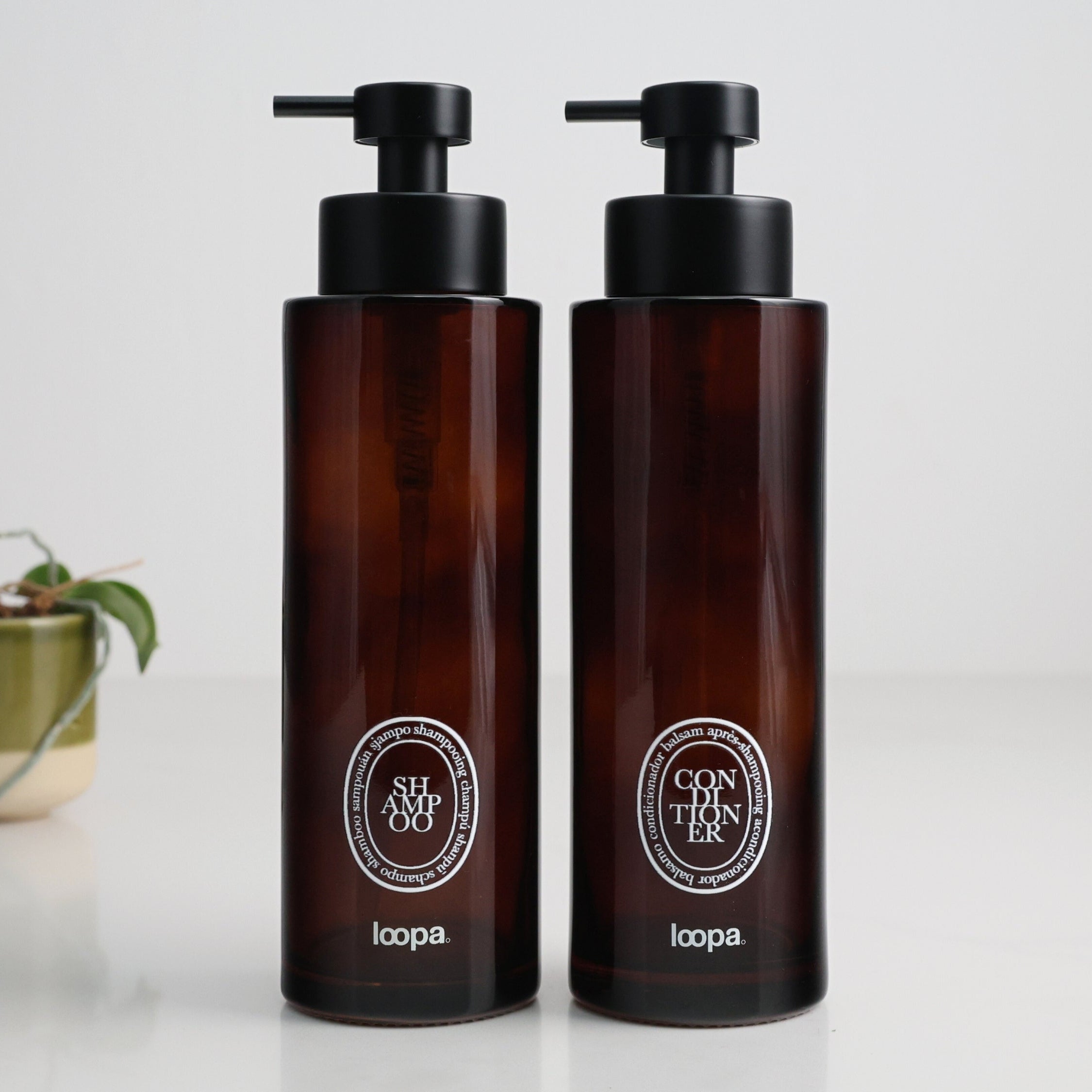 Two amber glass round bottle dispensers with white oval labels, presented as matching 500ml refillable options for soap or lotion use