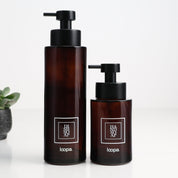 Two amber glass round bottle dispensers with white square labels, shown together in 500ml and 250ml refillable sizes for soap or lotion