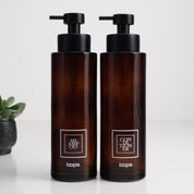 Two amber glass round bottle dispensers with white square labels, shown as matching 500ml refillable options for soap or lotion