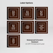 Amber glass round bottle dispenser displaying a selection of white square labels for organising refillable soap, lotion, shampoo, or conditioner