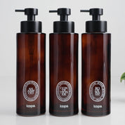 Three amber glass round bottle dispensers with white oval labels, shown together as matching 500ml refillable options for soap or lotion