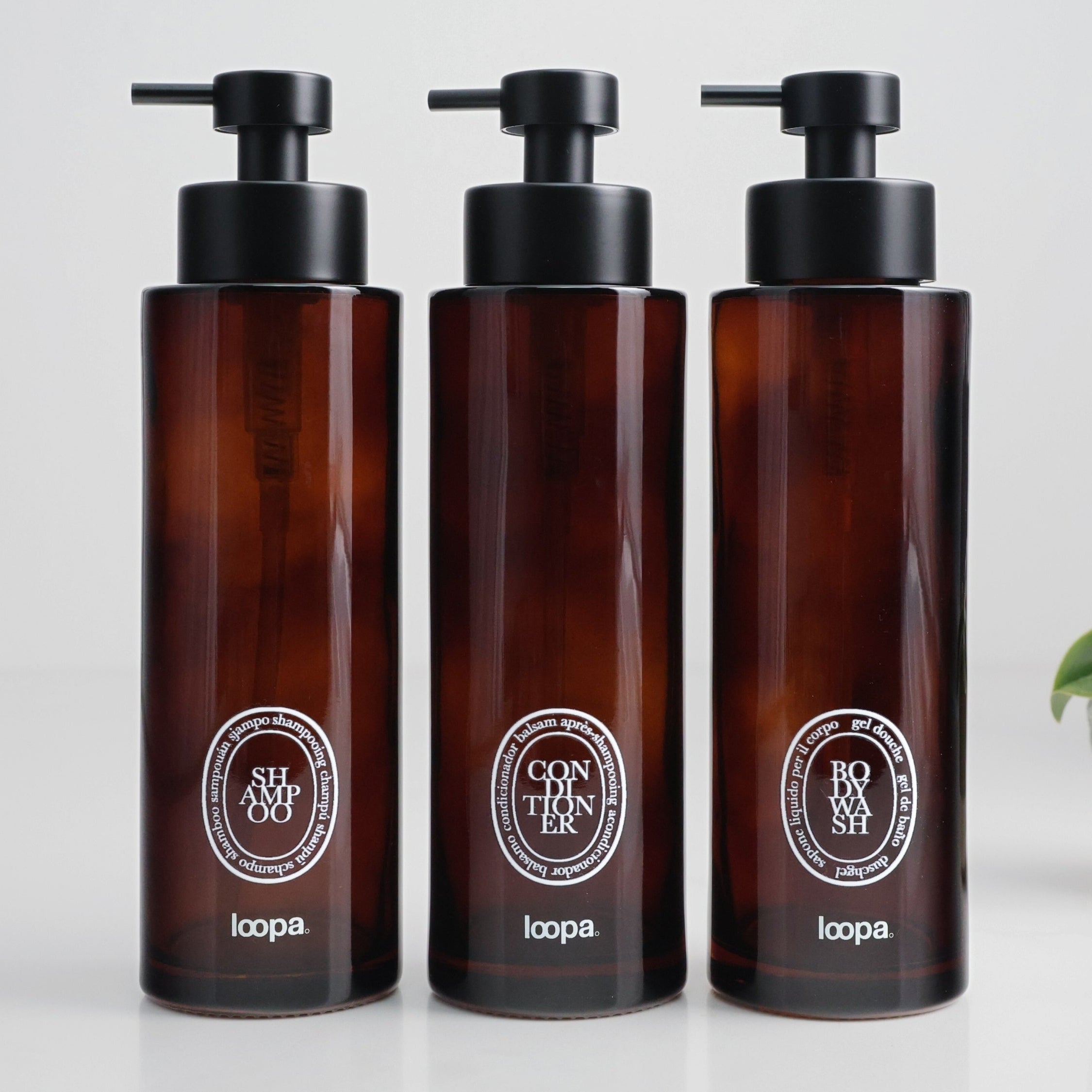 Three amber glass round bottle dispensers with white oval labels, shown together as matching 500ml refillable options for soap or lotion