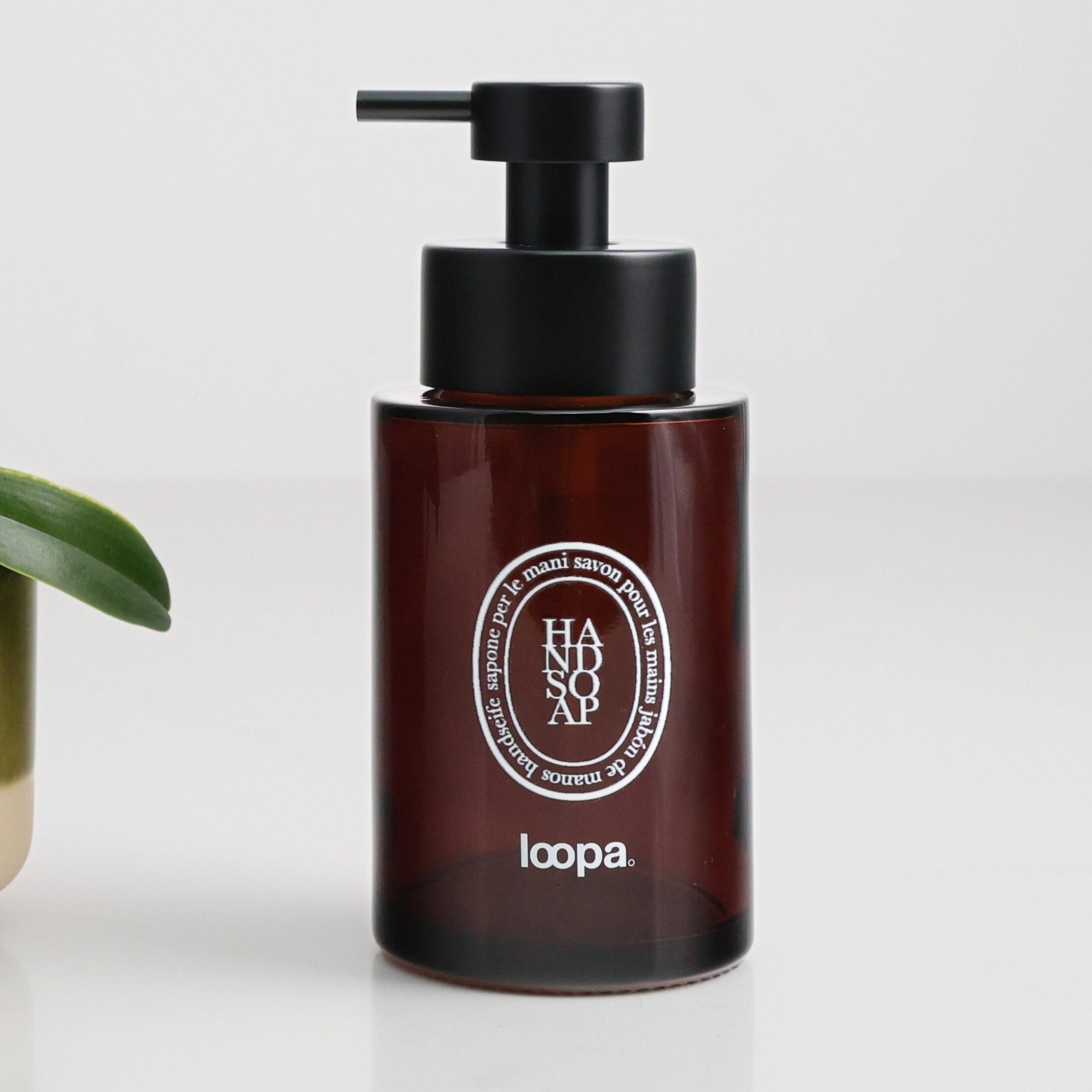 Amber glass round bottle dispenser with a white oval label, shown as a 250ml refillable bottle designed for bathrooms, cloakrooms, or WC settings