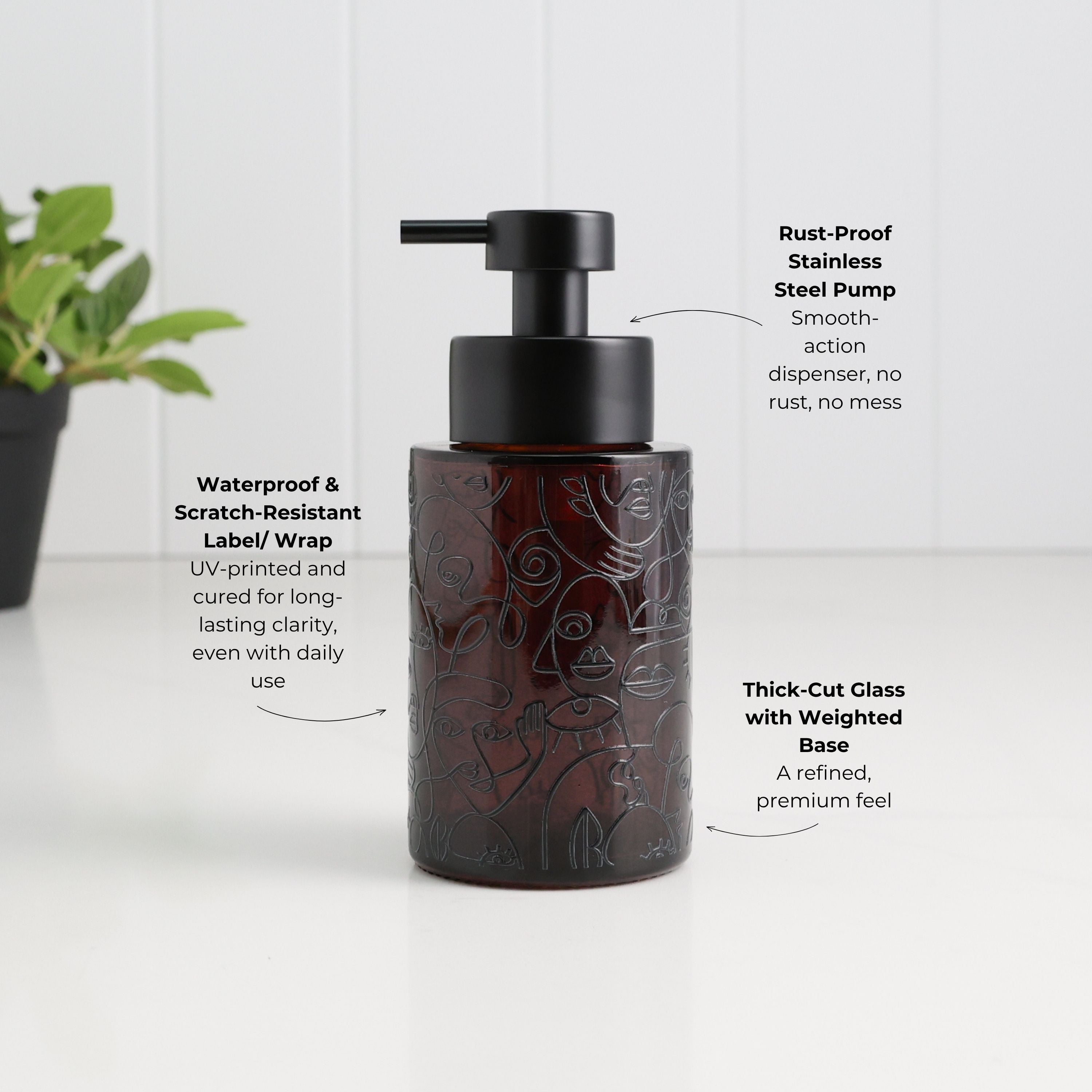A dark amber glass pump bottle with a black pump dispenser, shown on a white surface with decorative text callouts describing its features. A blurred green plant is visible on the left side.