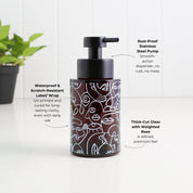 A dark brown cylindrical pump bottle with a black pump dispenser, featuring white line art illustrations of faces. The bottle is shown on a white surface with a white paneled background, with text callouts highlighting its features: 'Rust-Proof Stainless Steel Pump', 'Waterproof & Scratch-Resistant Label/Wrap', and 'Thick-Cut Glass with Weighted Base'.