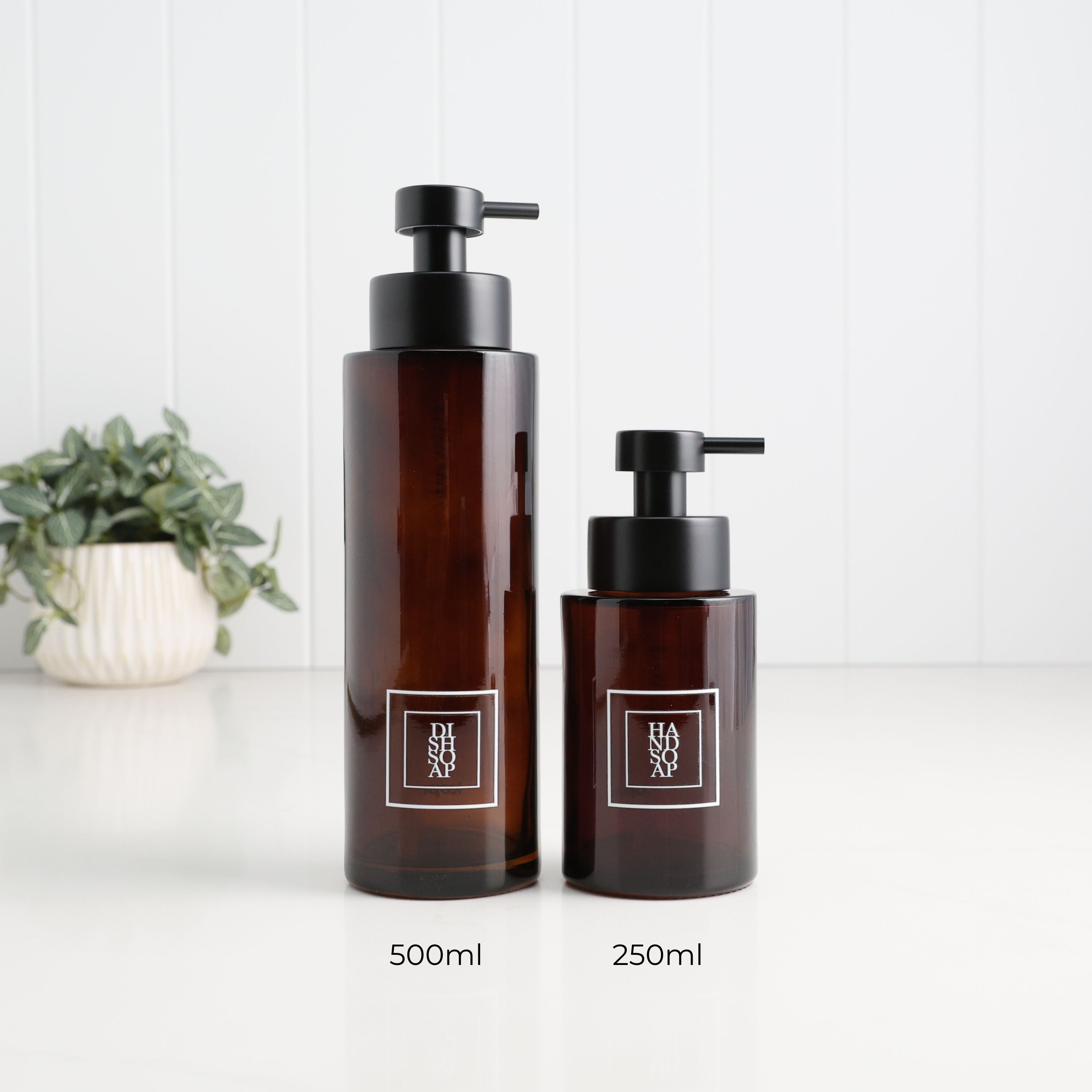 500ml and 250ml amber glass soap dispensers with white square dish soap and hand soap labels and satin black pumps, showing the two refillable bottle sizes side by side.