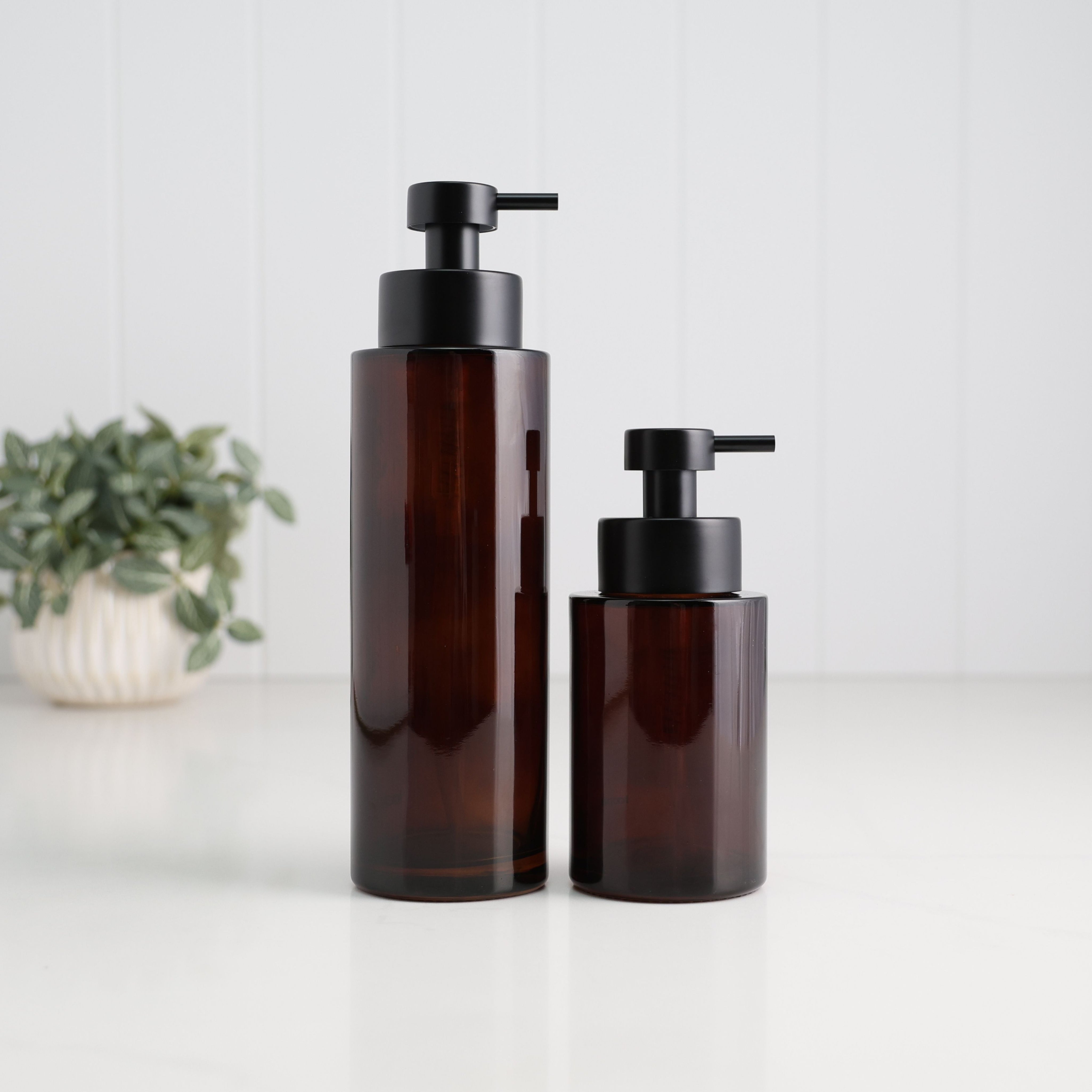 500ml and 250ml amber glass refillable soap dispensers shown together with satin black stainless steel liquid pumps, highlighting the two bottle sizes available for bathroom, kitchen or ensuite use.