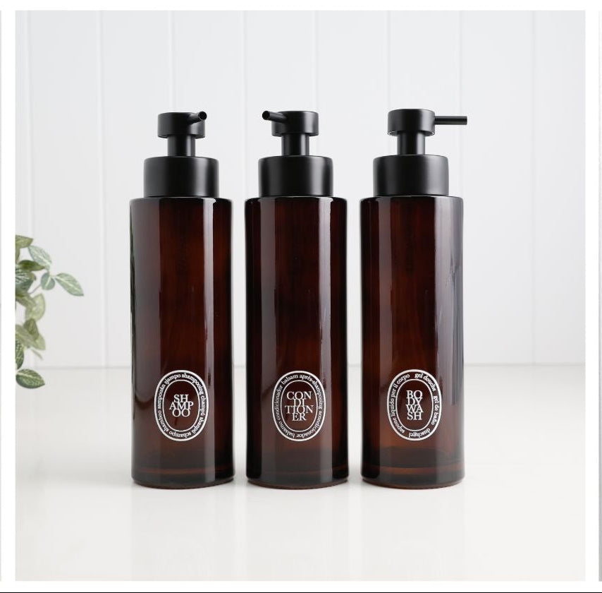 Four pump bottles shown in a four-panel collage on a white background, including matte silver, dark brown, white with black, and colorful tropical floral designs.