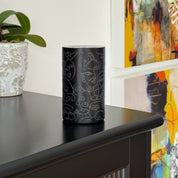 Loopa black rechargeable waterless essential oil diffuser with intricate grey abstract face line art, displayed on a black cabinet beside a decorative plant and colourful artwork. A stylish portable aromatherapy diffuser for modern living rooms, bedrooms and home interiors.