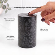Loopa black cordless waterless essential oil diffuser with grey abstract face pattern, showing a finger operating the top touch controls. Features three adjustable fragrance intensity levels, selectable 1, 2 or 3 hour run times and automatic shut-off three hours after the last button press. Rechargeable aromatherapy diffuser for personalised home fragrance.