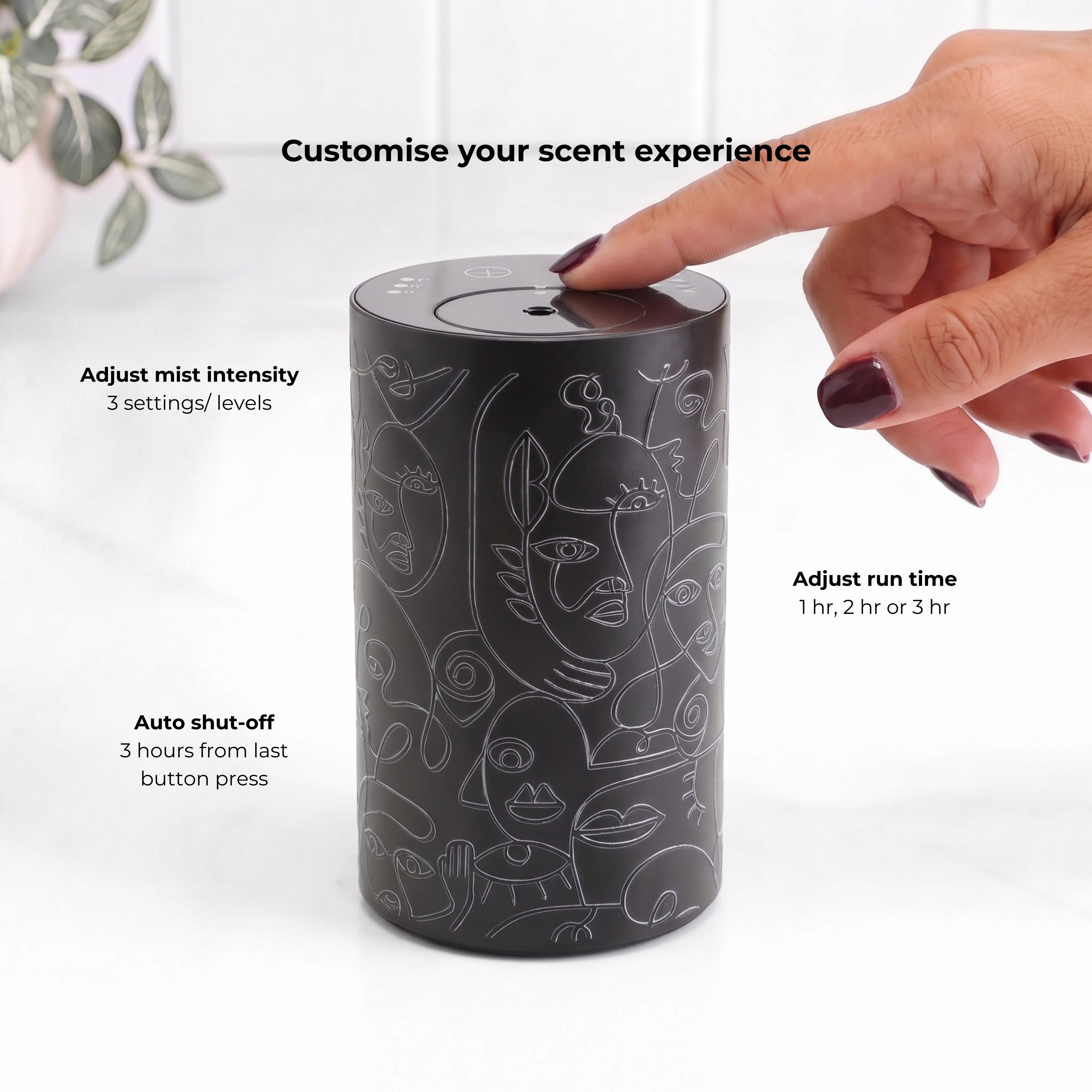 Loopa black cordless waterless essential oil diffuser with grey abstract face pattern, showing a finger operating the top touch controls. Features three adjustable fragrance intensity levels, selectable 1, 2 or 3 hour run times and automatic shut-off three hours after the last button press. Rechargeable aromatherapy diffuser for personalised home fragrance.