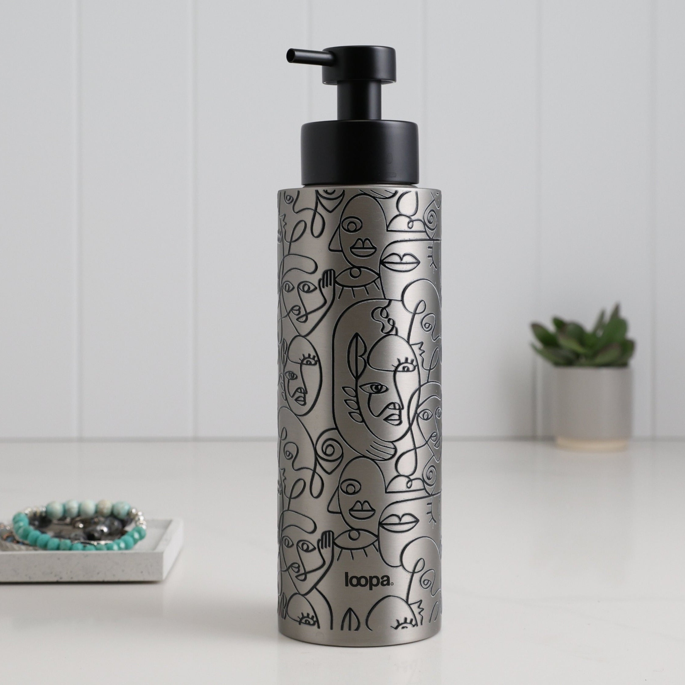 Brushed stainless steel round bottle dispenser with a black wrap label, shown as a 500ml refillable bottle suited to contemporary kitchen or bathroom spaces