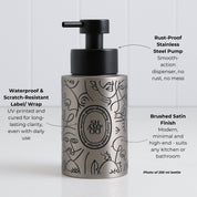 Brushed stainless steel round bottle dispenser with a boho-style black label featuring arrow artwork, shown as a 250ml refillable option for soap or lotion