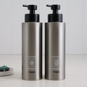 Brushed stainless steel round bottle dispensers with white square labels, shown as a mixed 500ml and 250ml refillable pairing for contemporary sink spaces