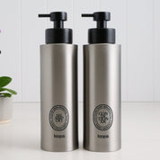 Two brushed stainless steel round bottle dispensers with black oval labels, shown as matching 500ml refillable bottles suited to bathrooms, cloakrooms, or kitchen counters