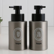 Two brushed stainless steel round bottle dispensers with white oval labels, shown as matching 250ml refillable bottles suited to cloakrooms, WC spaces, or compact bathrooms