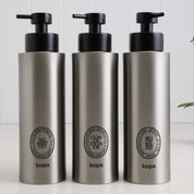 Three brushed stainless steel round bottle dispensers with black oval labels, arranged as matching 500ml refillable bottles for bathrooms, showers, or modern kitchen spaces
