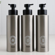 Three brushed stainless steel round bottle dispensers with white oval labels, arranged as matching 500ml refillable bottles for bathrooms, showers, or modern kitchen spaces