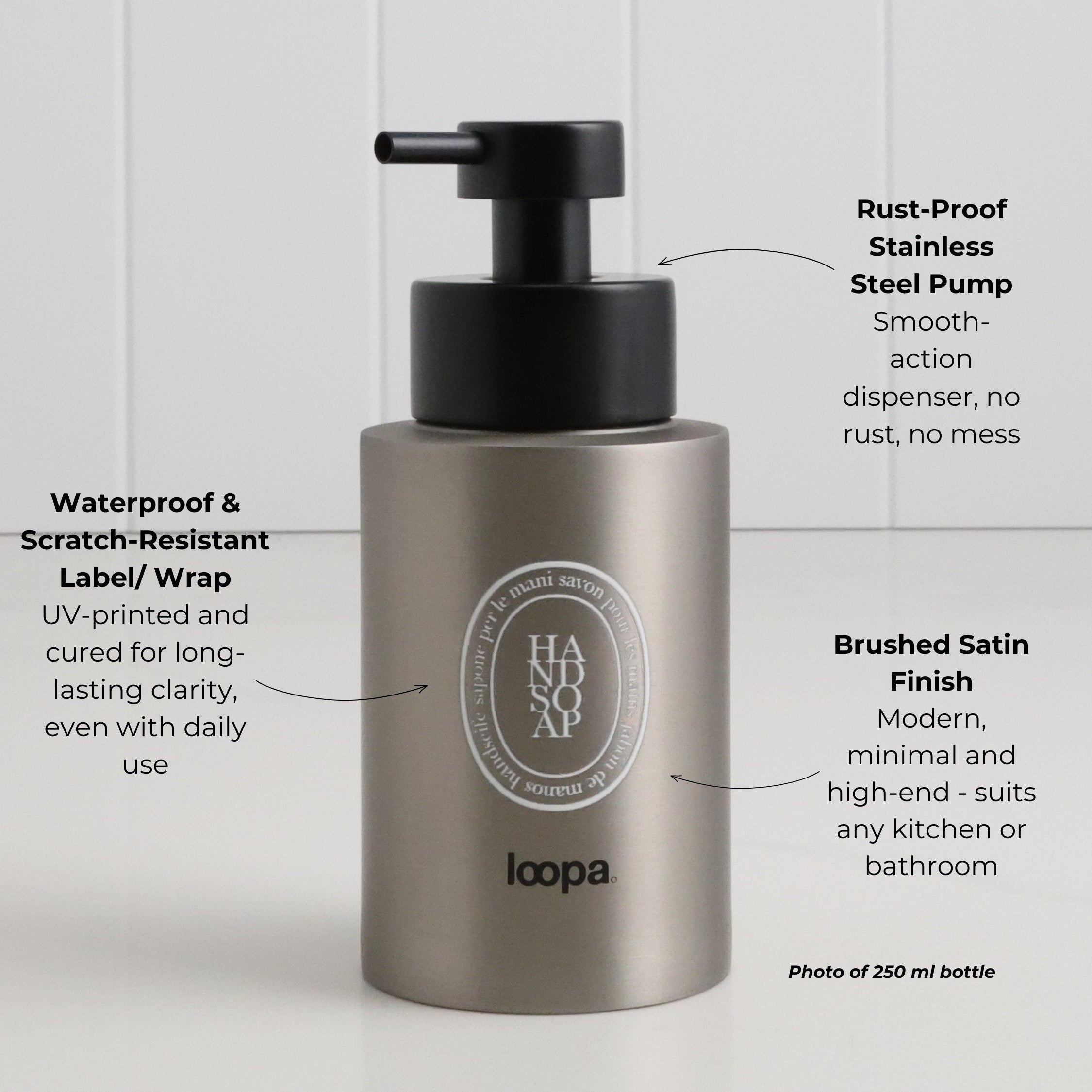 Brushed stainless steel round bottle dispenser with a white oval label featuring arrow detailing, suited to bathrooms, kitchens, or shower spaces