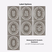 Brushed stainless steel round bottle dispenser showing white oval label options, intended for organising refillable bottles across kitchens, bathrooms, cloakrooms, or WC spaces