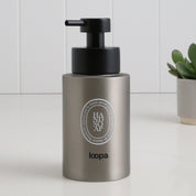 Brushed stainless steel round bottle dispenser with a white oval label, shown as a 250ml refillable bottle designed for cloakrooms, WC areas, or compact bathrooms