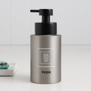 Brushed stainless steel round bottle dispenser with a white square label, shown as a 250ml refillable bottle suited to cloakroom, WC, or bathroom settings