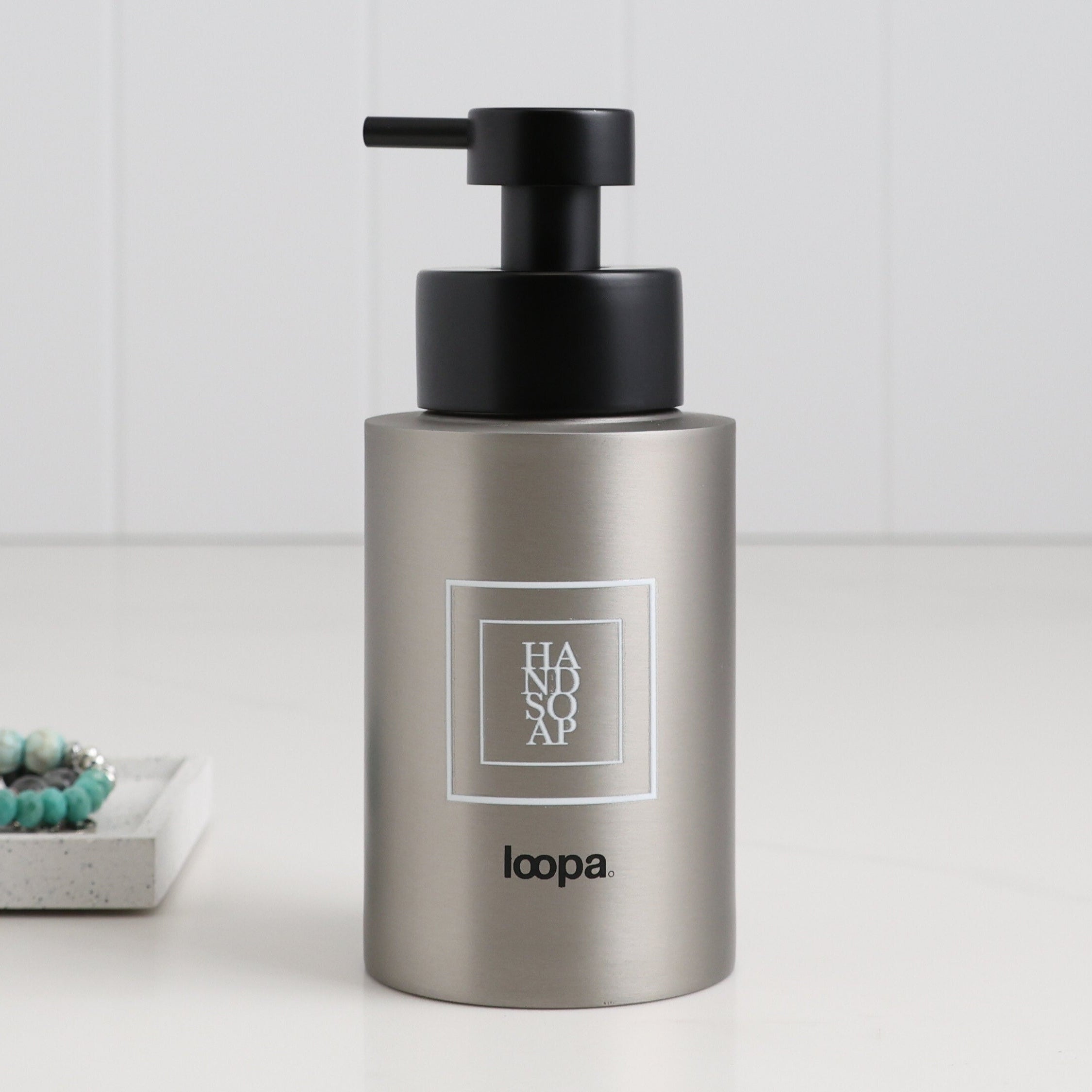 Brushed stainless steel round bottle dispenser with a white square label, shown as a 250ml refillable bottle suited to cloakroom, WC, or bathroom settings