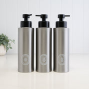 Set of three 500ml brushed 304 stainless steel dispensers for shampoo, conditioner and body wash, finished with white oval labels and satin black liquid pumps for a coordinated bathroom or shower set.