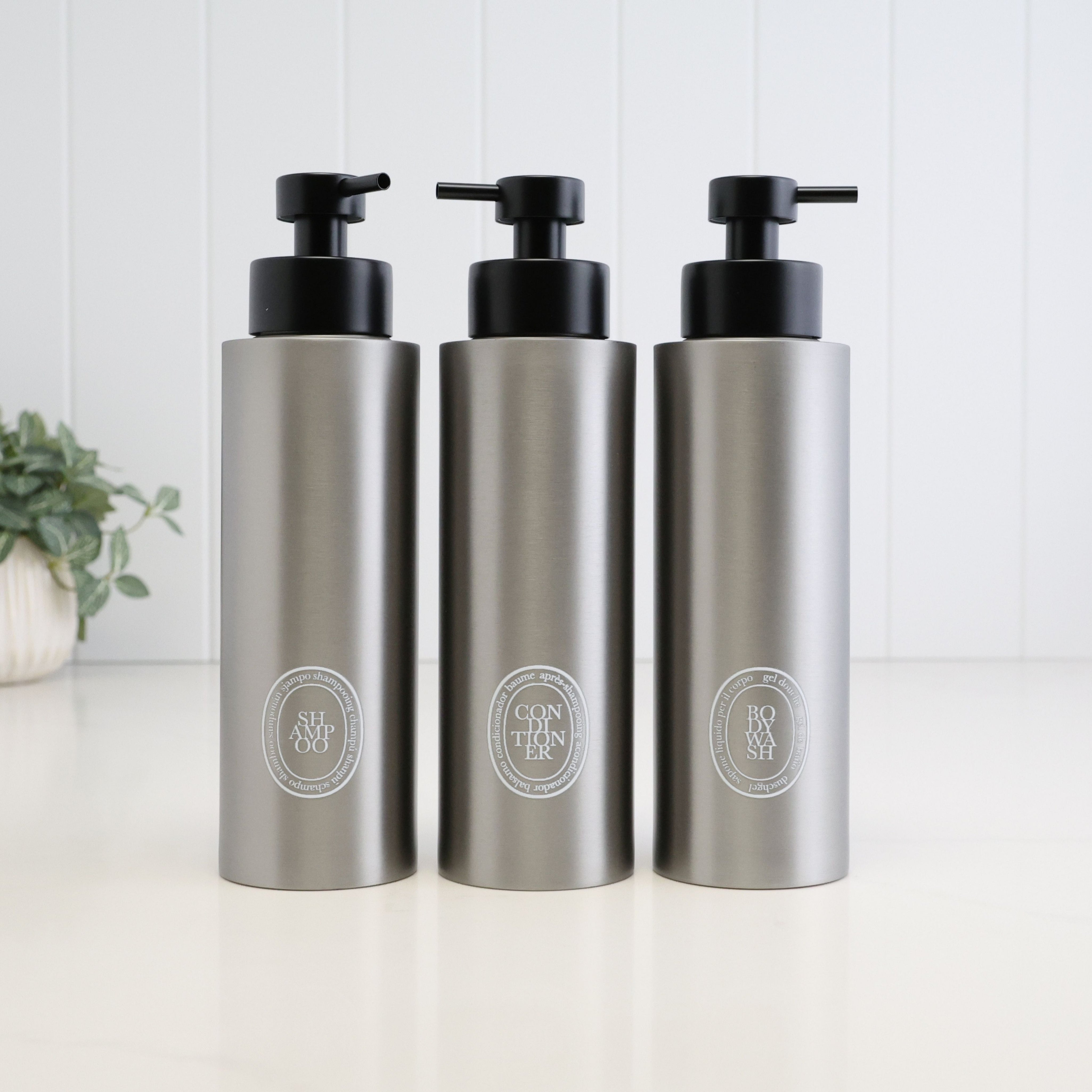 Set of three 500ml brushed 304 stainless steel dispensers for shampoo, conditioner and body wash, finished with white oval labels and satin black liquid pumps for a coordinated bathroom or shower set.
