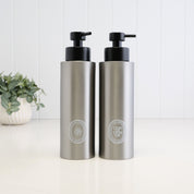 Pair of 500ml brushed 304 stainless steel shampoo and conditioner dispensers with white oval UV-DTF labels and satin black liquid pumps, designed as a refillable bathroom and shower bottle set.